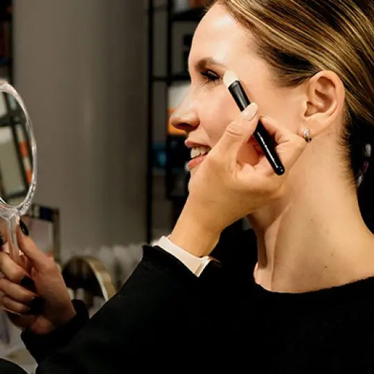 Applying makeup while looking in a hand mirror